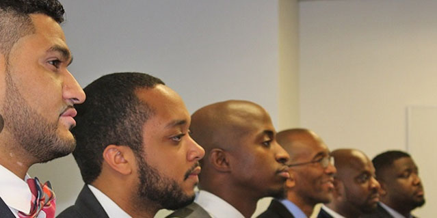 several African American men in profile and suits appearing to be listening to a speaker