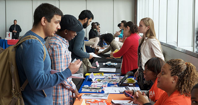 students speaking with people at a table with flyers