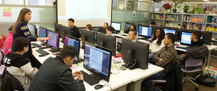 students sitting at computers and a teacher speaking to them