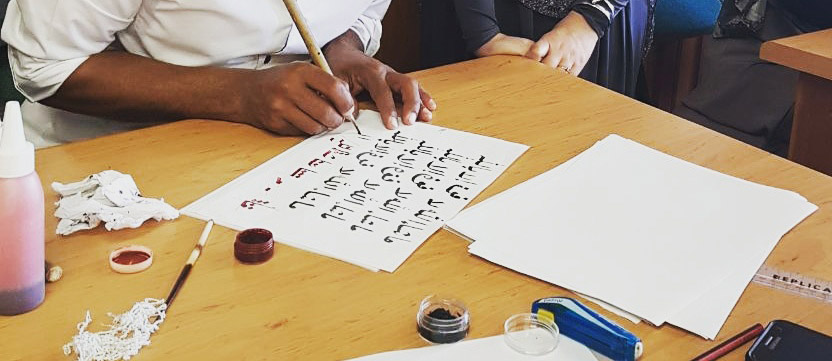 student's hands practicing Arabic calligraphy