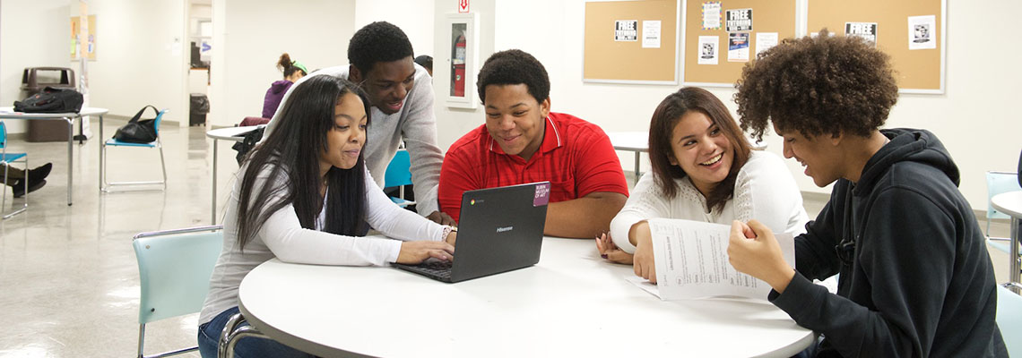 Several students with laptops sitting at a table talking