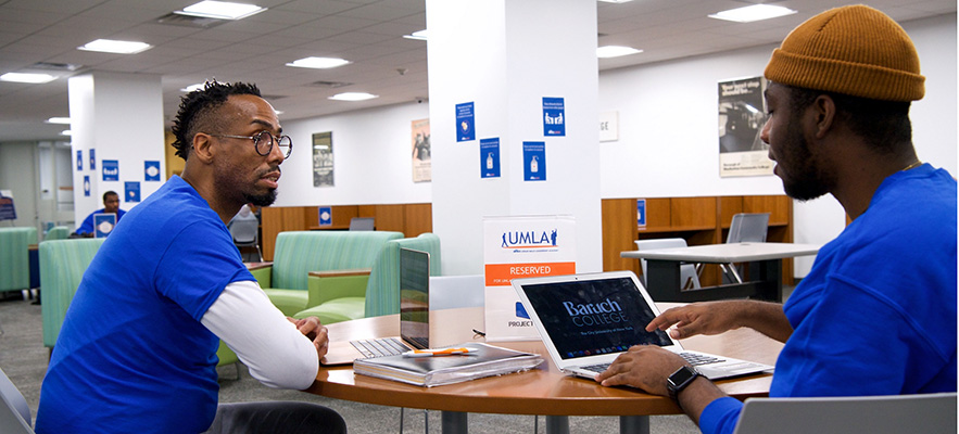 two male students sitting at a table talking with a laptop on the table